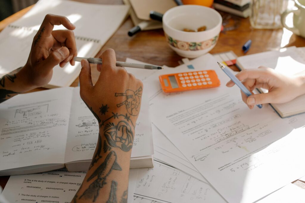 Person With Tattoo on Arm Holding Pen Writing on White Paper